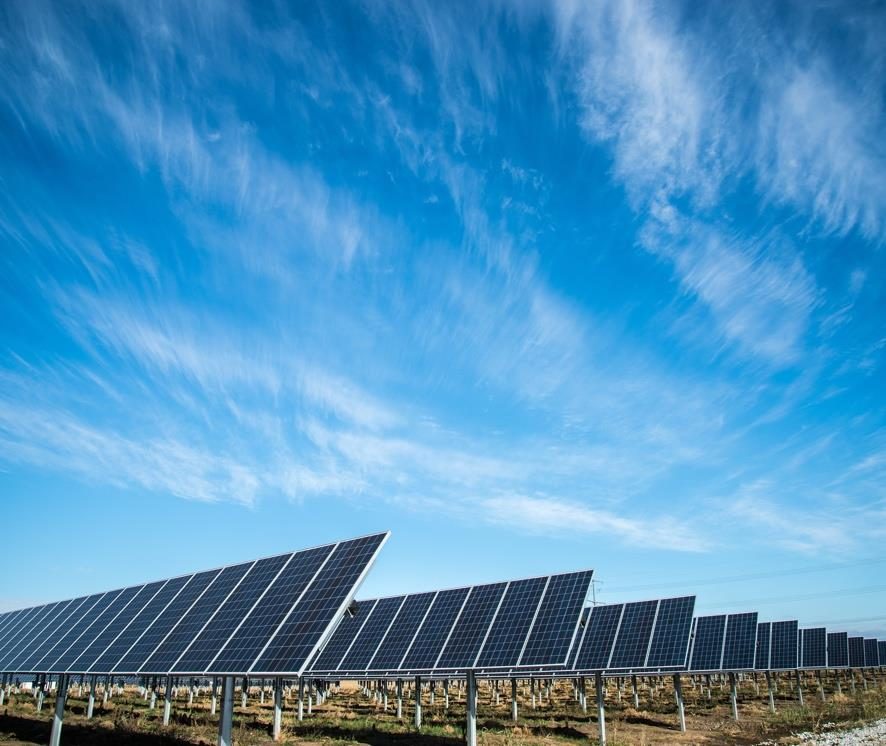 A row of solar panels tracking the sun beneath a wide blue sky